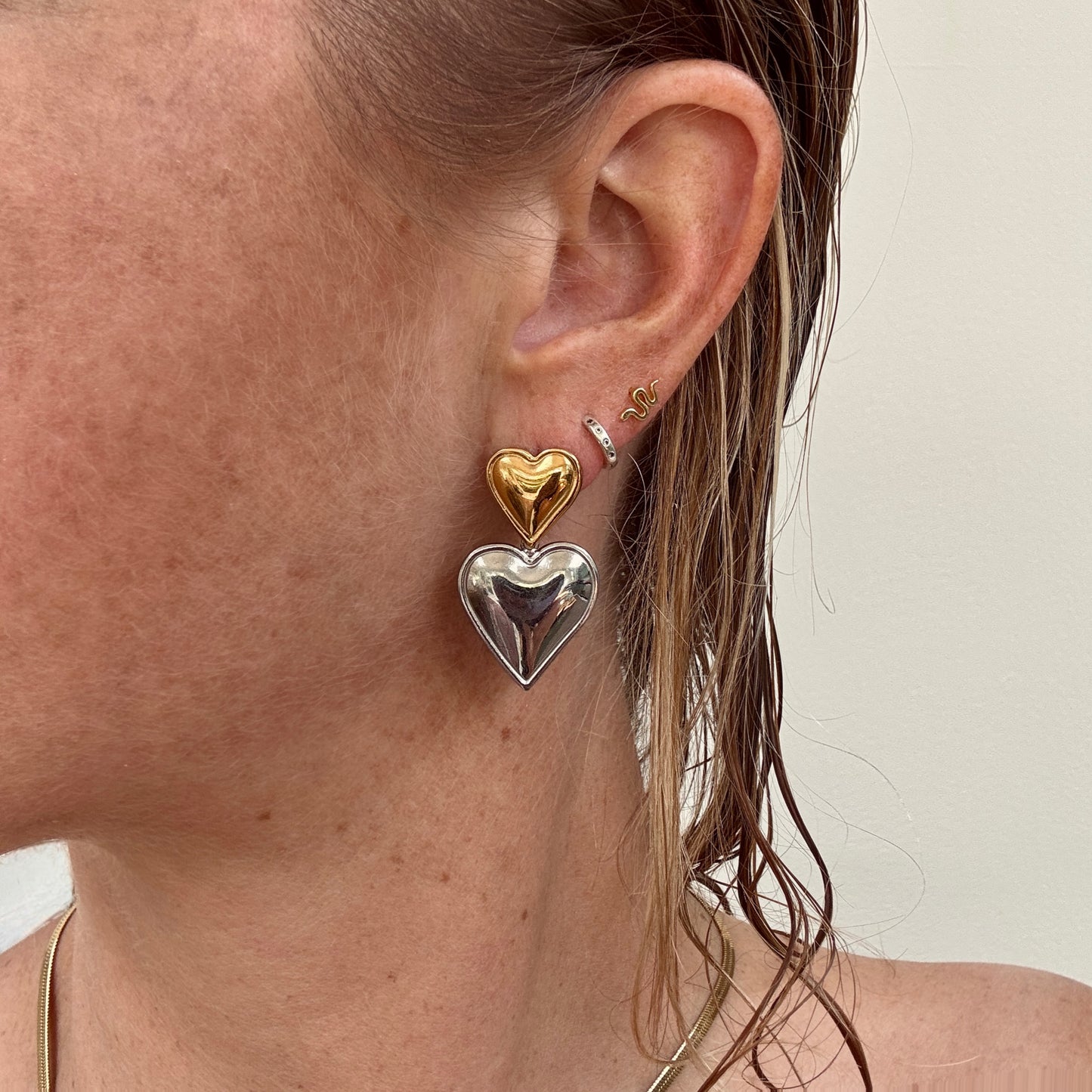 Double Heart Dangly Earrings in Silver and Gold worn on ear.