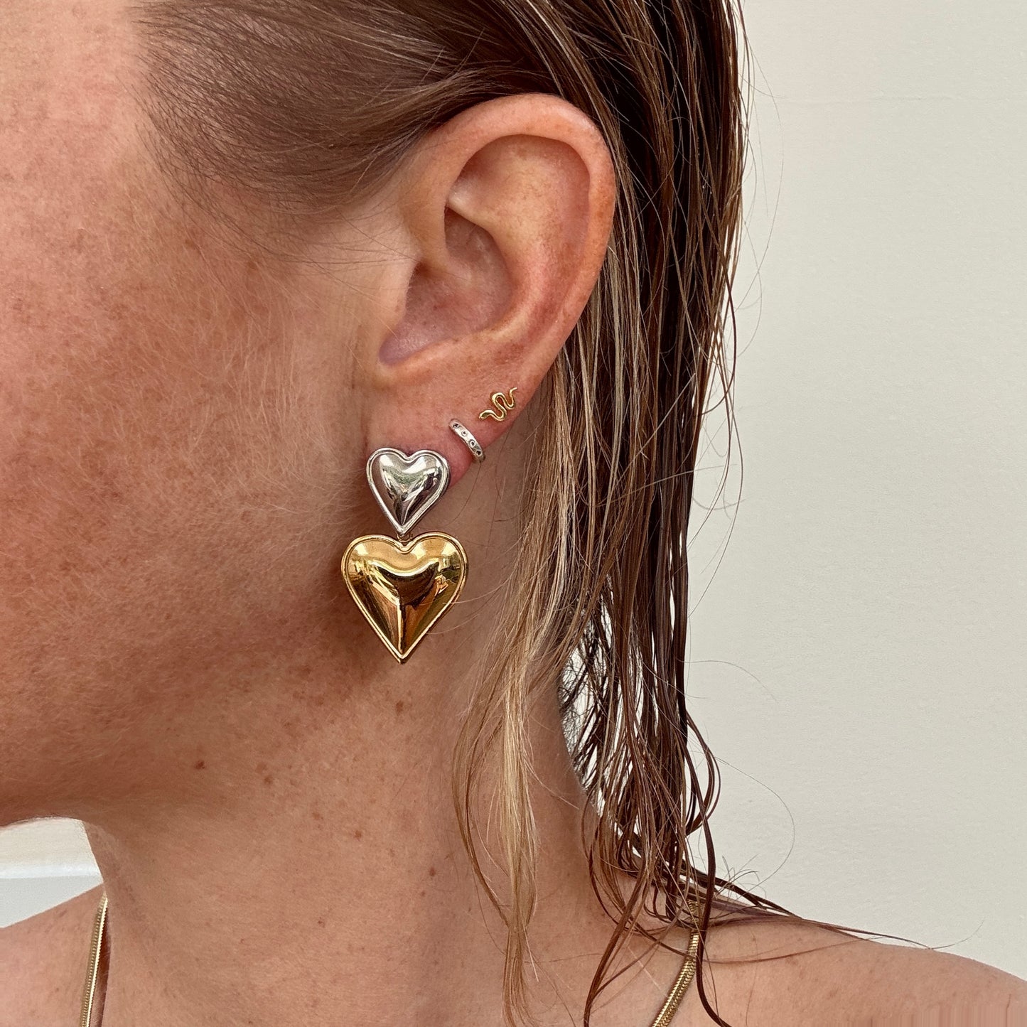 Double Heart Dangly Earrings in Gold and Silver worn on ear.