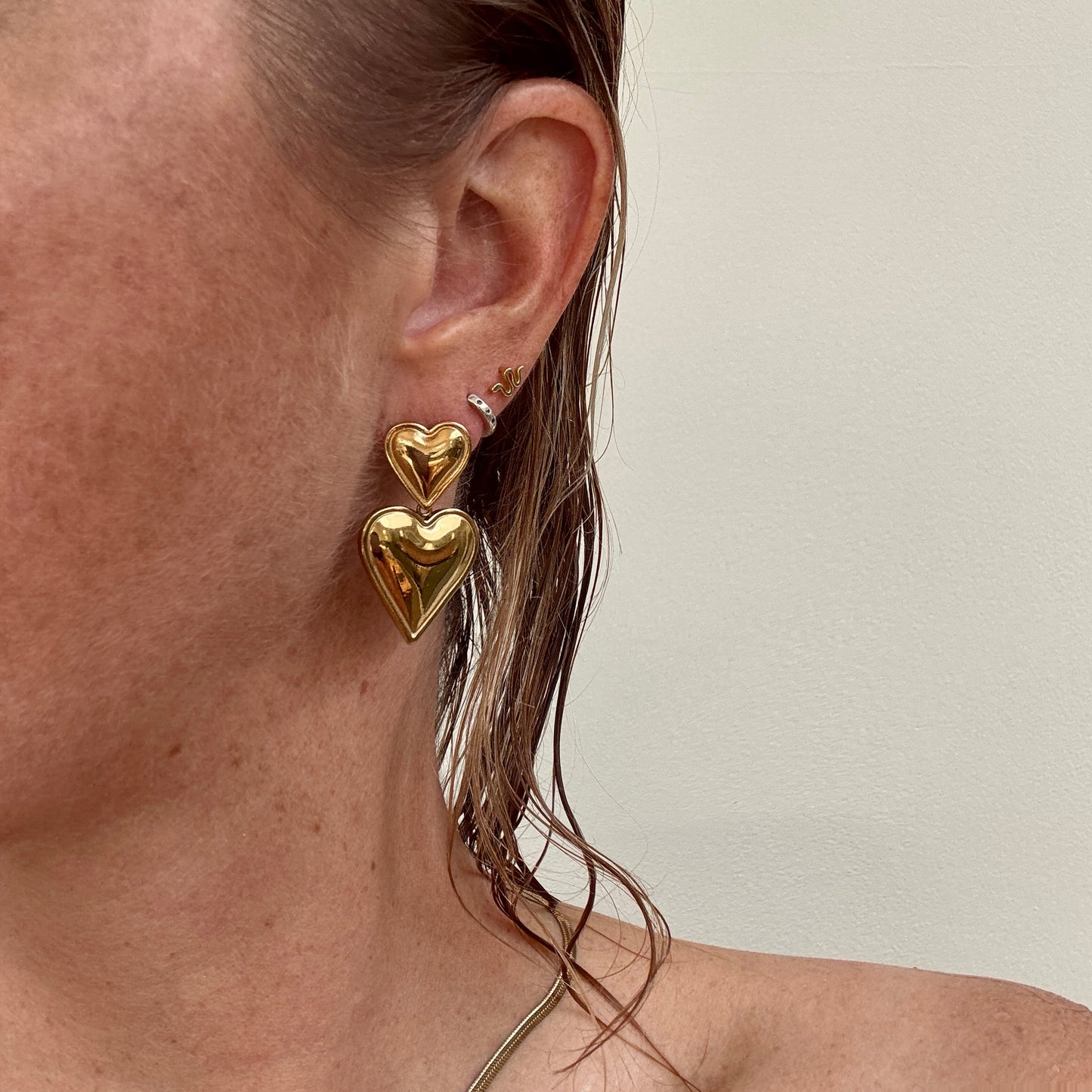 Double Heart Dangly Earrings in Gold, worn on ear.