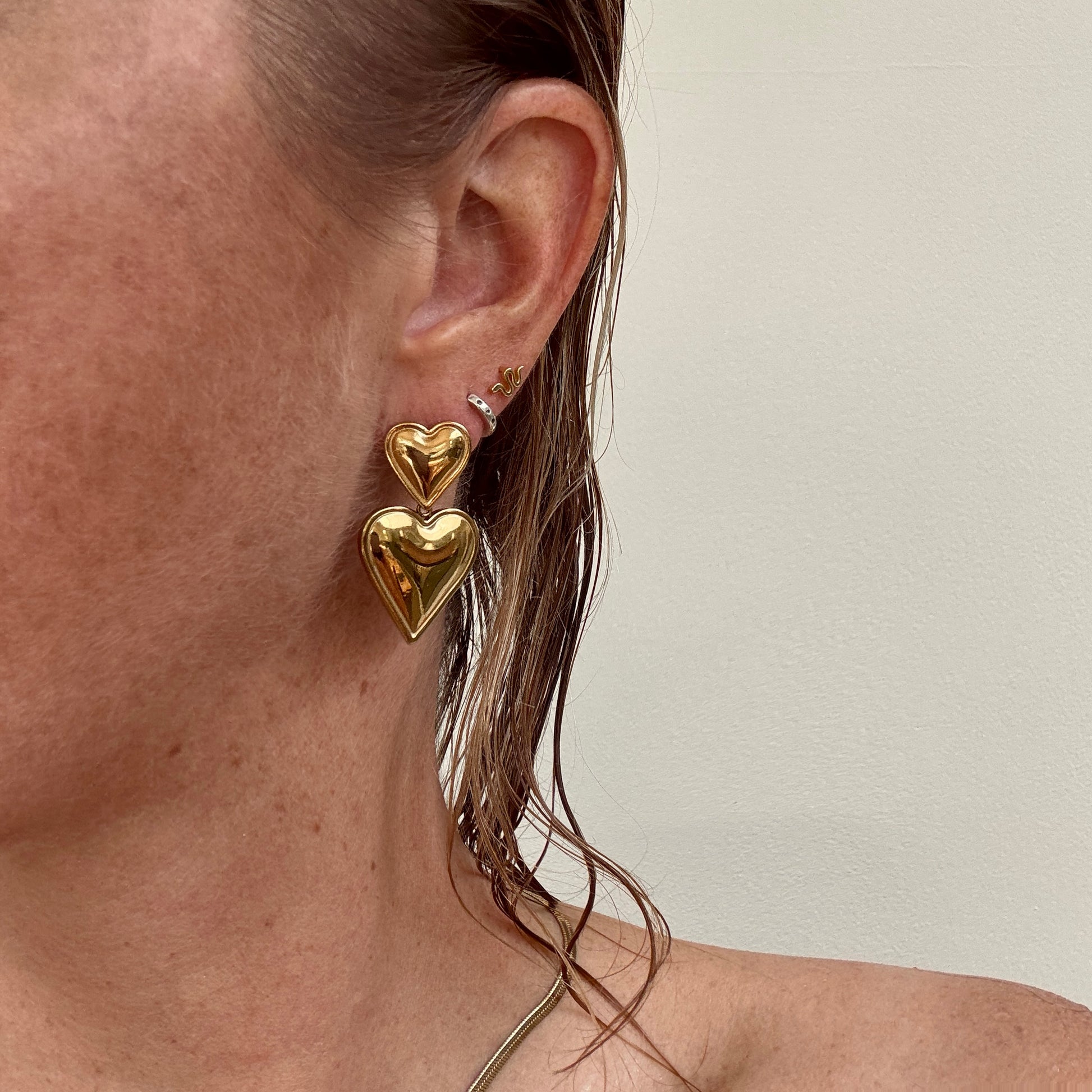 Double Heart Dangly Earrings in Gold, worn on ear.